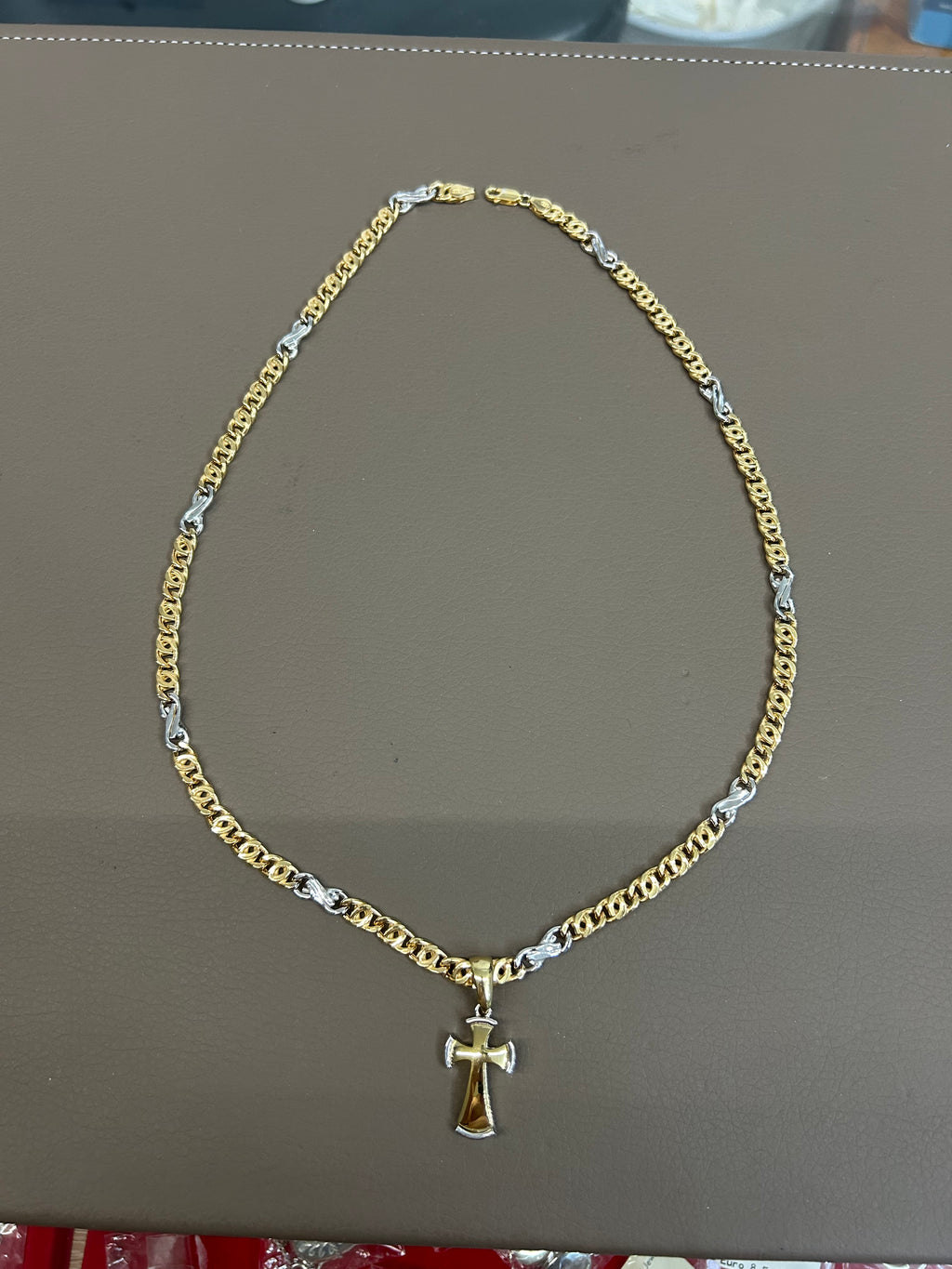 Collana in argento 925 placcato oro bicolore con ciondolo a croce, distesa su piano espositivo grigio