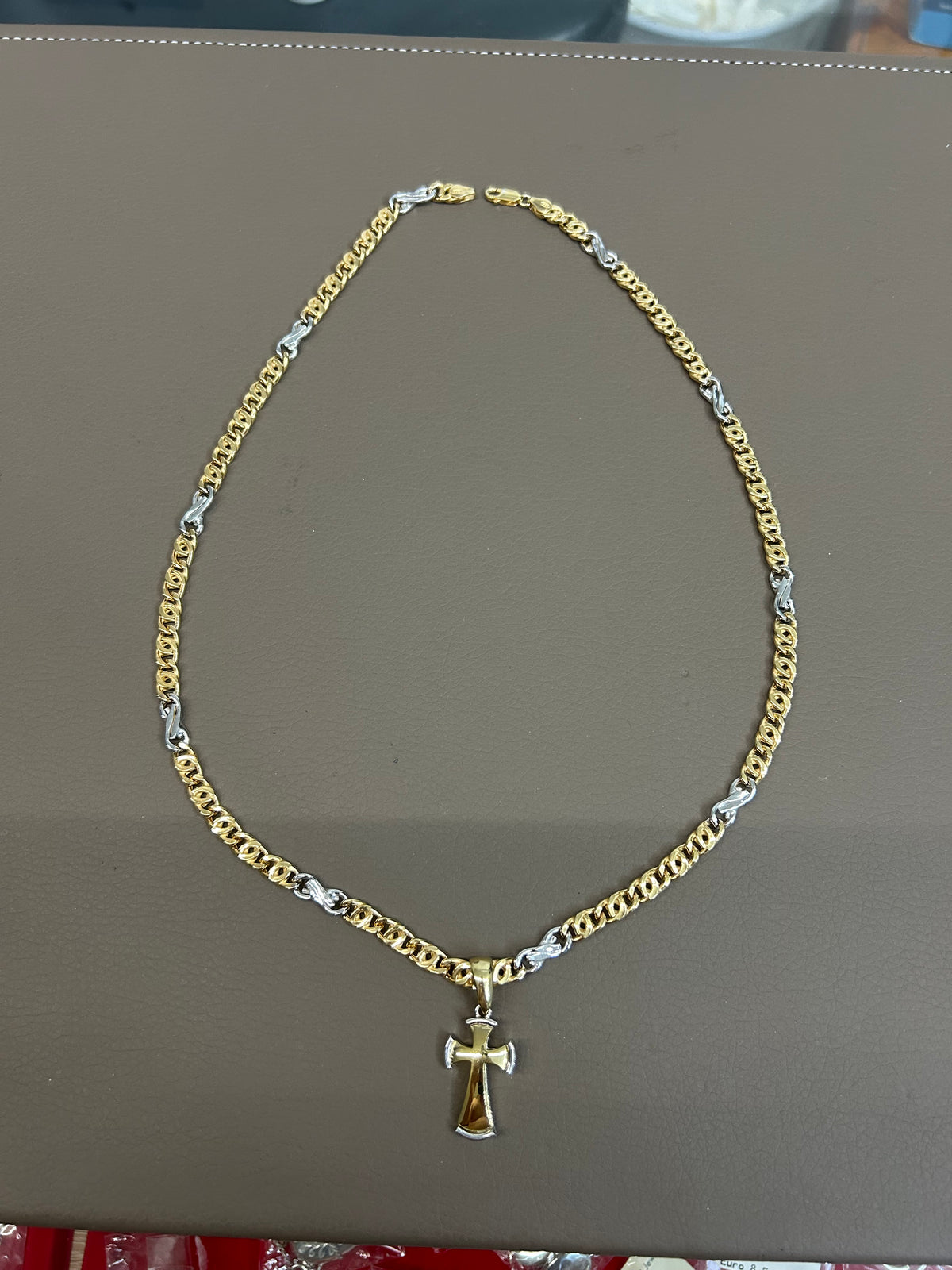 Collana in argento 925 placcato oro bicolore con ciondolo a croce, distesa su piano espositivo grigio