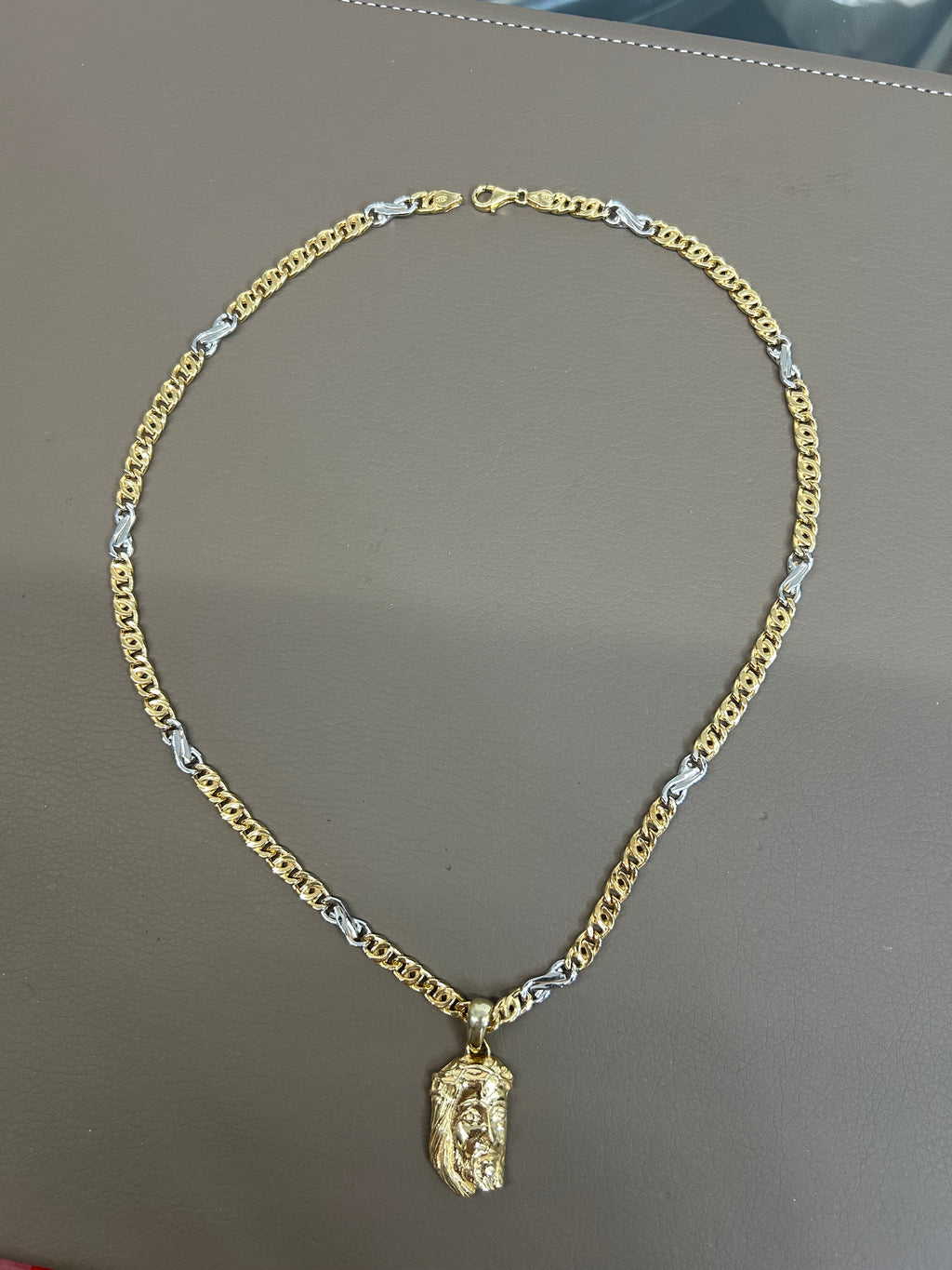 Collana bicolore con maglie dorate e argentate e ciondolo Volto di Cristo, distesa su piano grigio con chiusura a moschettone visibile