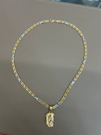 Collana bicolore con maglie dorate e argentate e ciondolo Volto di Cristo, distesa su piano grigio con chiusura a moschettone visibile